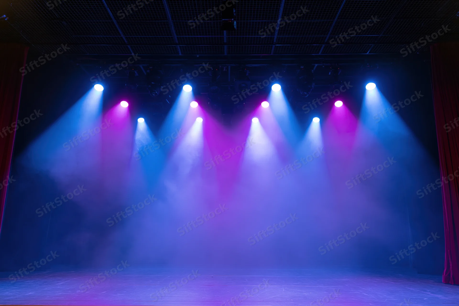 Empty theater stage illuminated by blue and purple spotlights with smoke, viewed from front of house