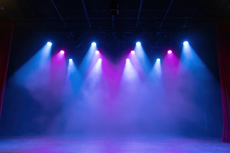 Empty theater stage illuminated by blue and purple spotlights with smoke, viewed from front of house