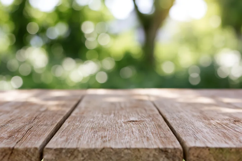 Weathered wooden tabletop in outdoor garden setting with blurred green foliage background