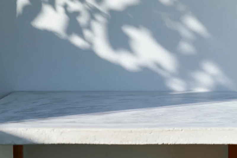 Empty white concrete shelf with leaf shadows on a plain wall outdoors
