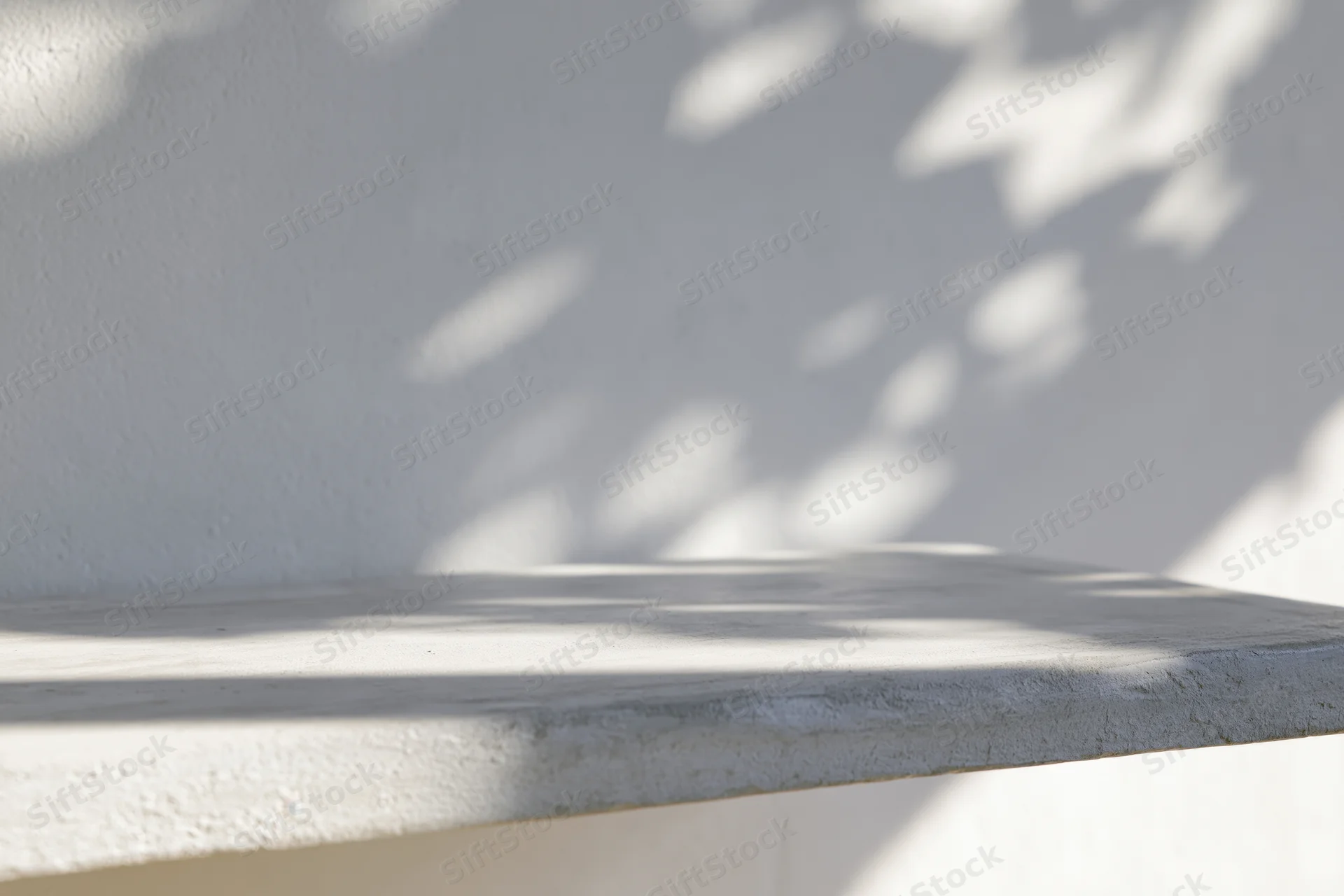 White concrete shelf with dappled leaf shadows on a plain wall outdoors