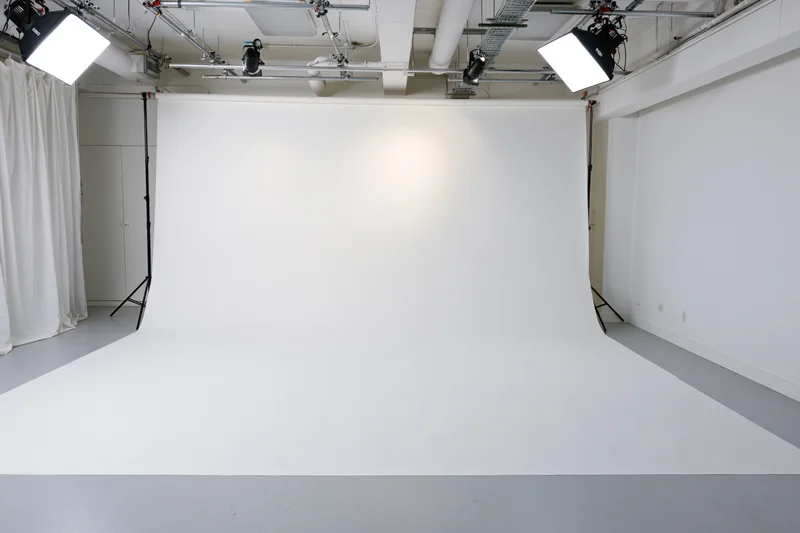 Empty white seamless backdrop in a photography studio with overhead lighting and gray floor