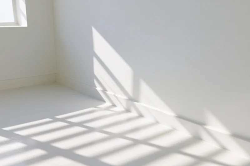 Empty white room with sunlight casting grid shadows on floor and wall