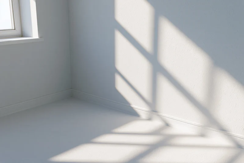Empty white room with sunlight casting shadows on bare walls and smooth floor