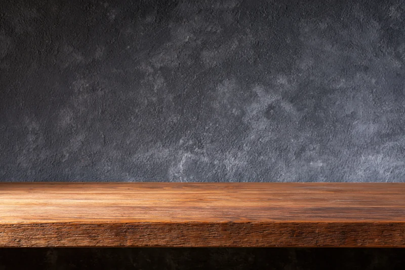 Empty wooden shelf against dark textured wall with copyspace for display