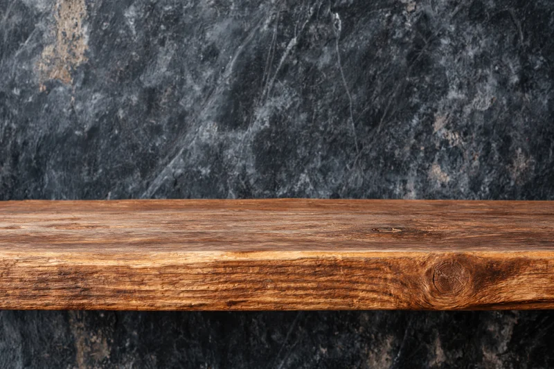 Empty worn wooden shelf surface against dark stone wall