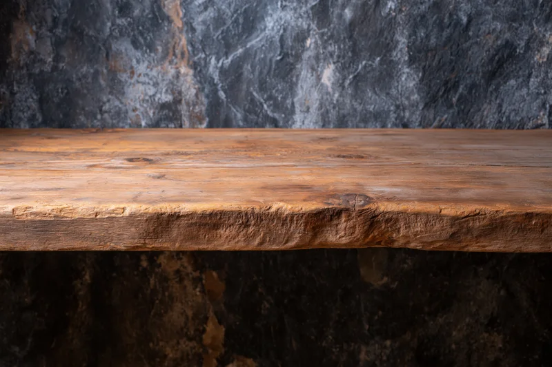 Empty worn wooden shelf with live edge against dark stone wall