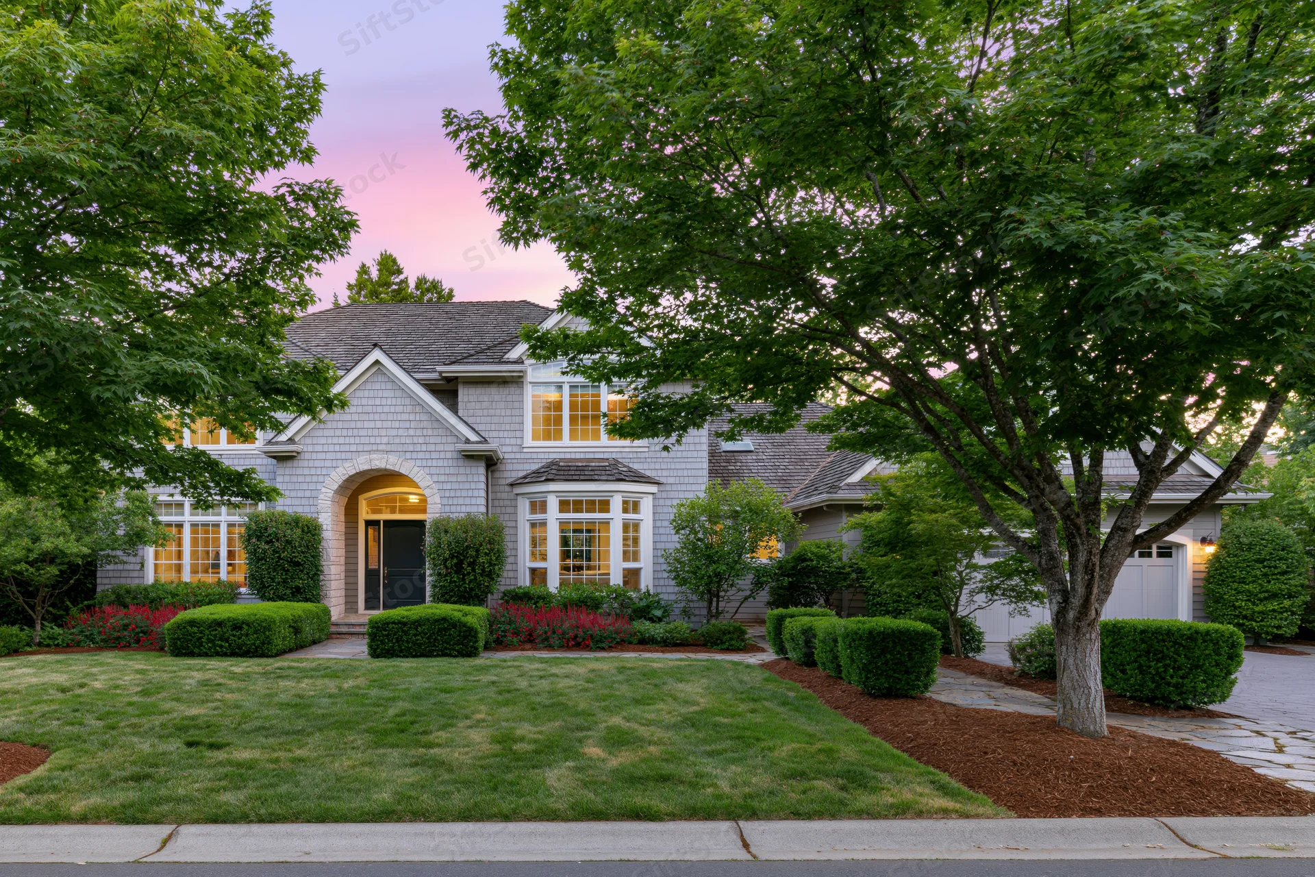 Large american suburban house with gray cedar shingle siding and landscaped front yard at dusk