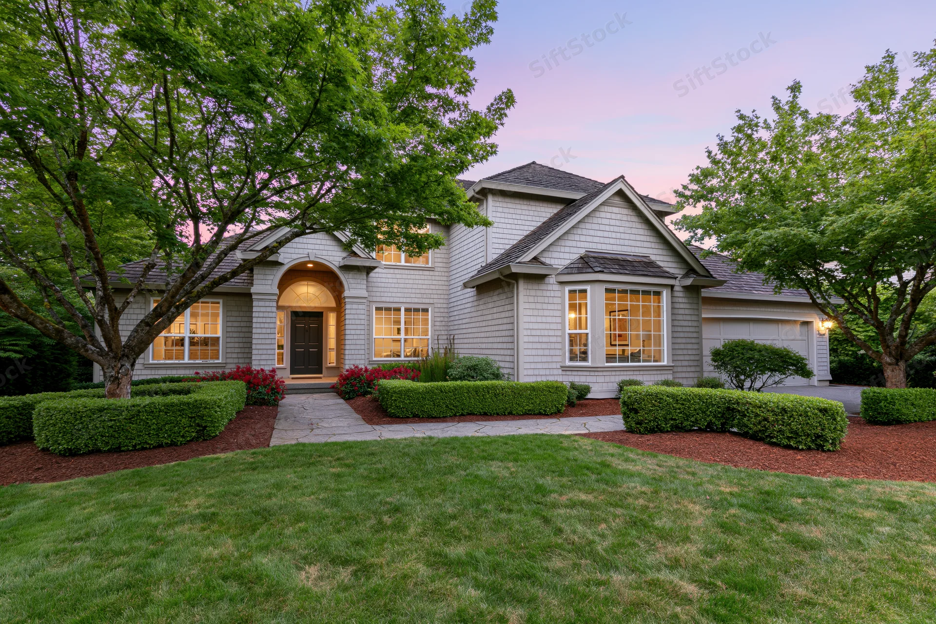 Gray cedar-sided suburban house exterior with arched entryway and landscaped front yard at dusk