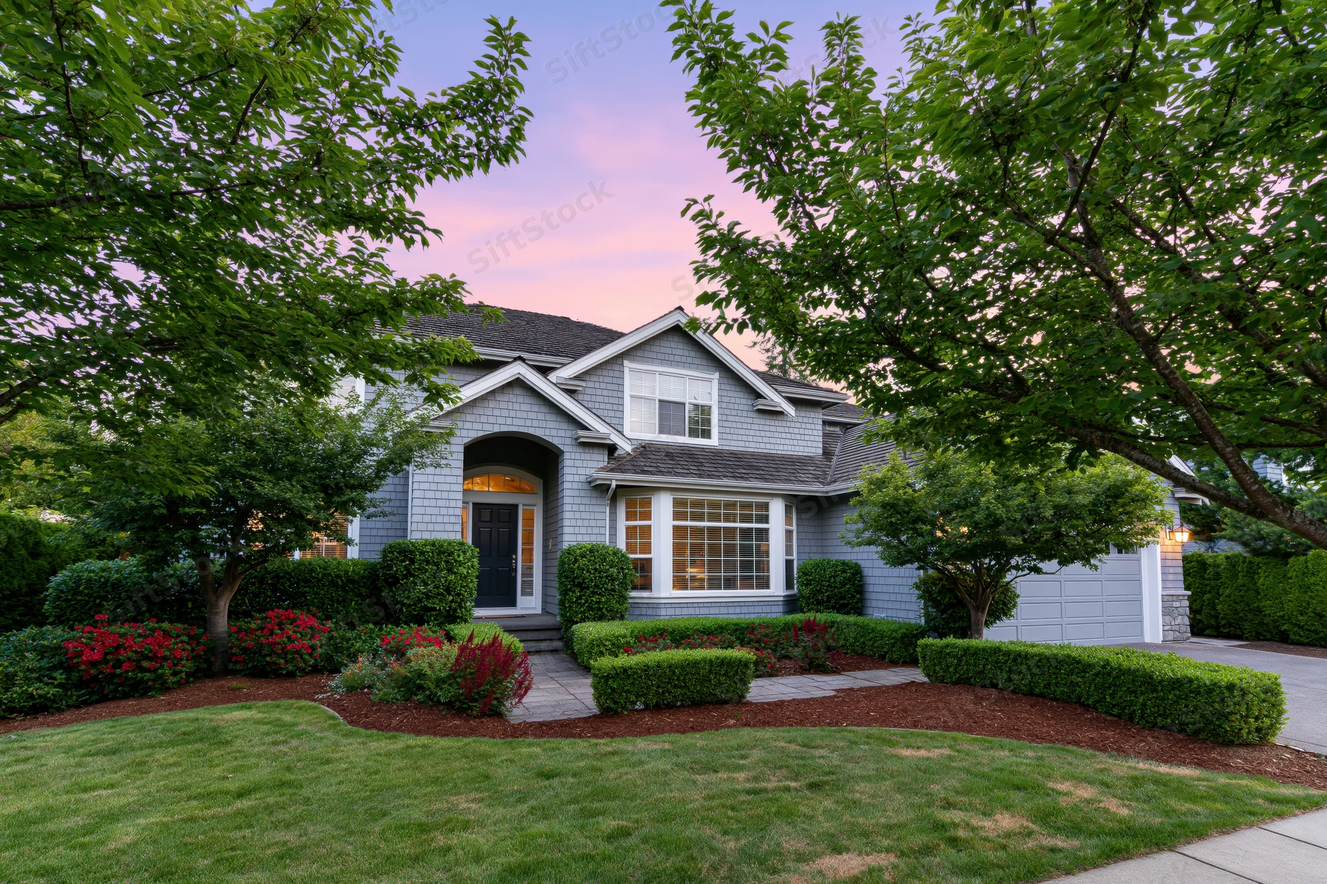 Large american suburban house with gray cedar siding and landscaped front yard at twilight