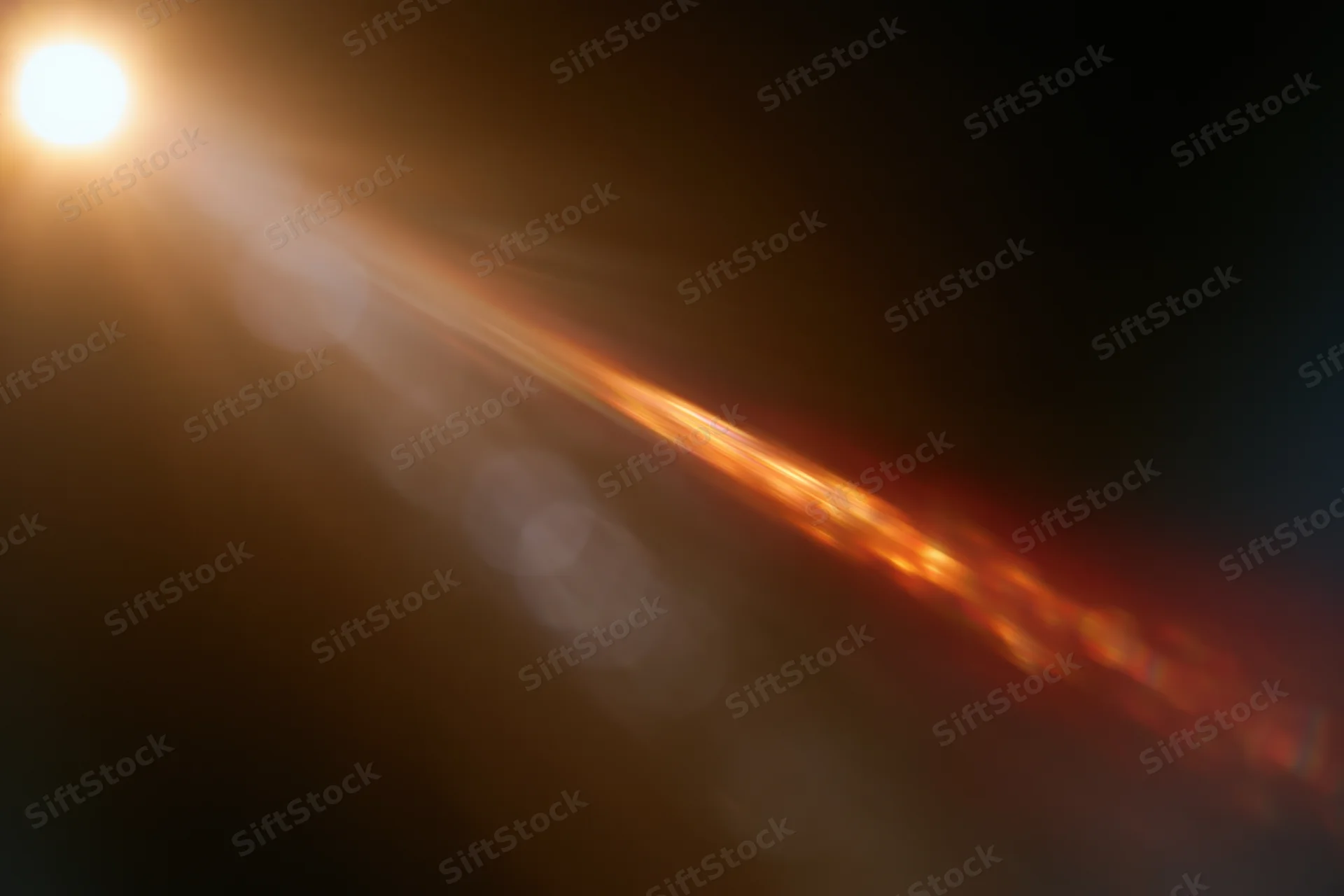 Bright warm light source creating abstract bokeh and lens flare streaks across dark background
