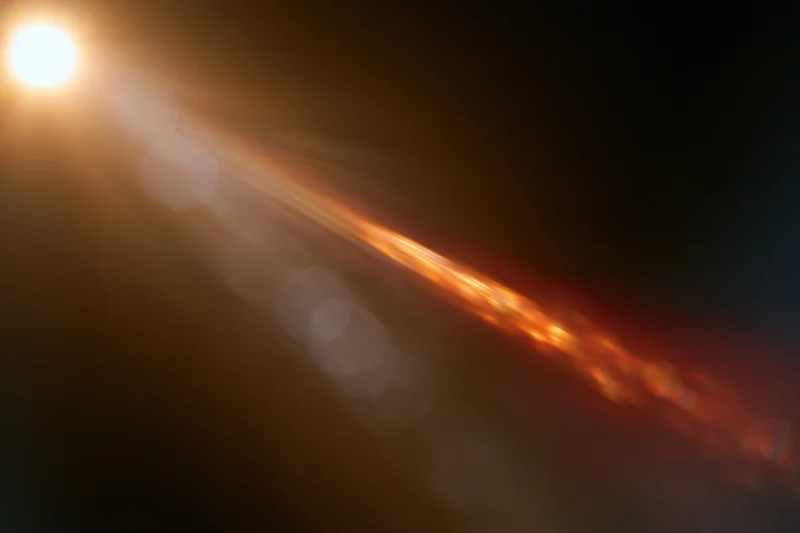 Bright warm light source creating abstract bokeh and lens flare streaks across dark background