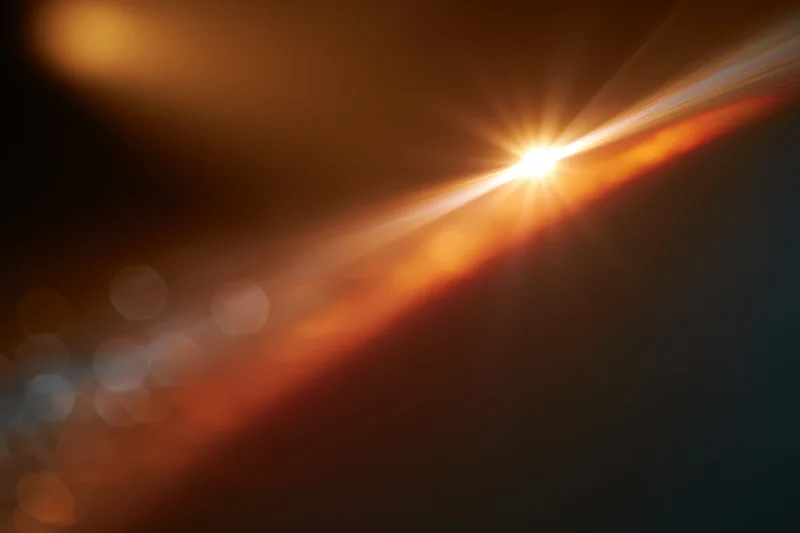 Bright warm light source creating abstract bokeh and lens flare against dark background