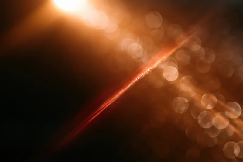 Warm light source creating abstract bokeh with lens flare and soft glow across dark background