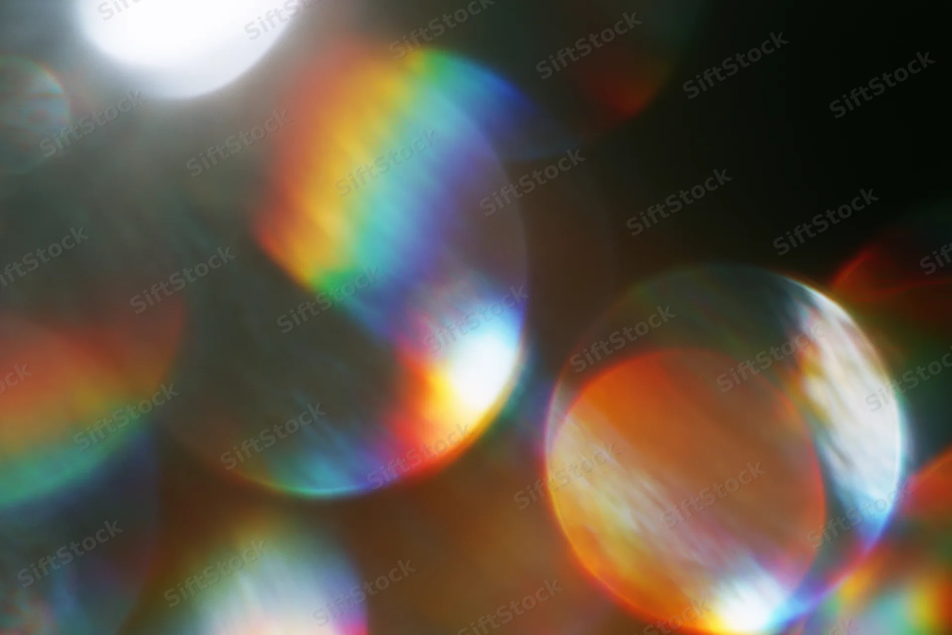 Abstract circular bokeh light scatter with rainbow iridescence against dark background
