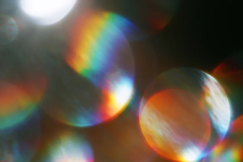 Abstract circular bokeh light scatter with rainbow iridescence against dark background