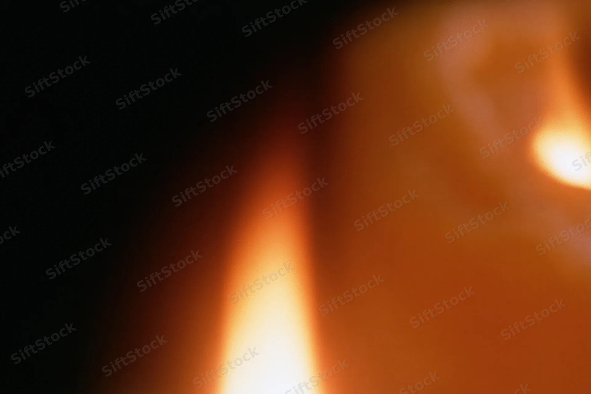 Close-up of a flickering candle flame in a dark room with warm glow and blurred background