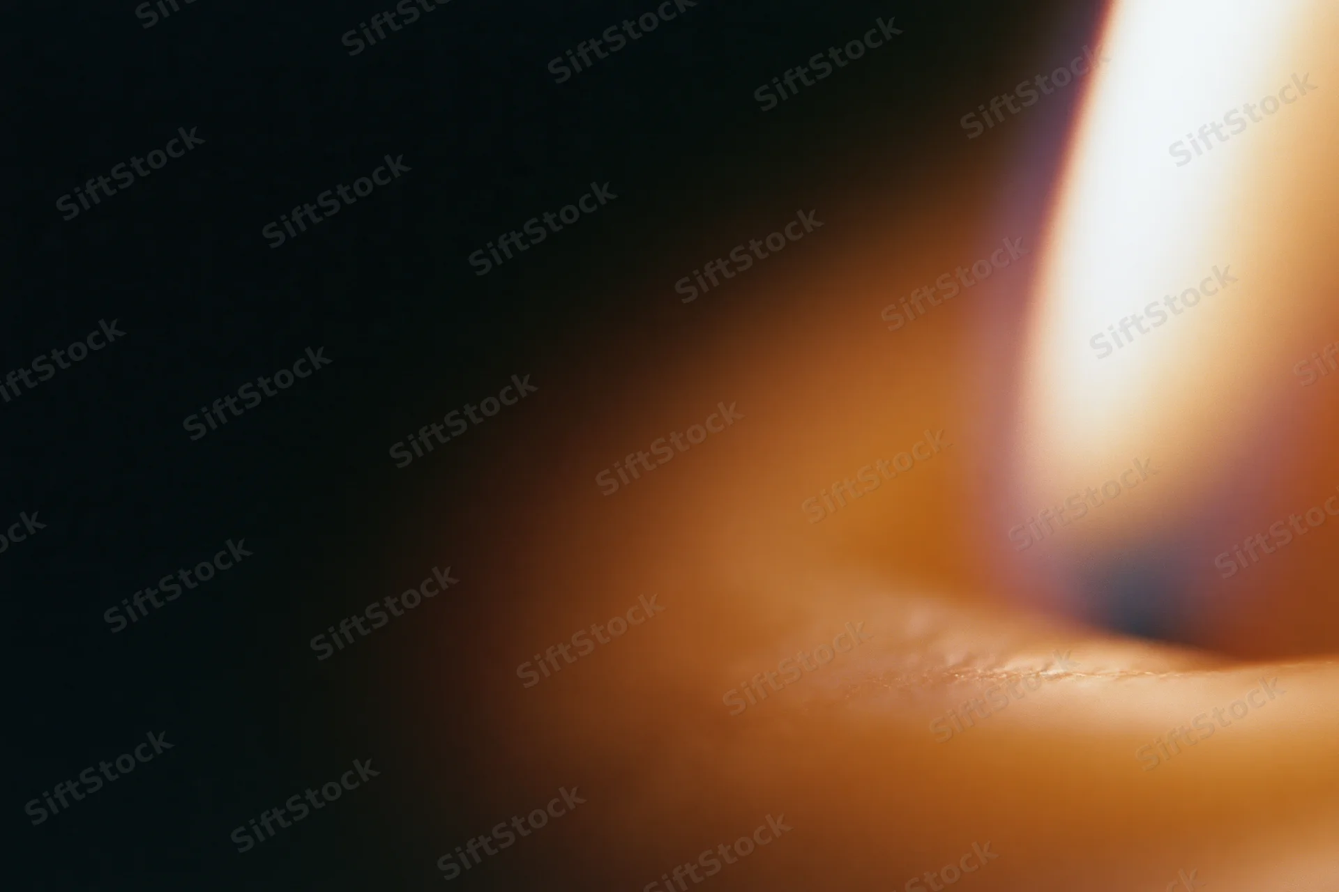 Close-up of a candle flame glowing warmly beside a blurred finger in soft focus