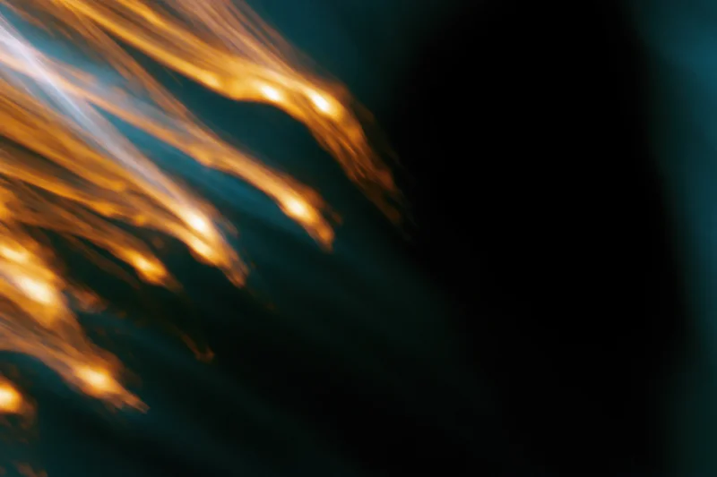 Warm amber light streaks moving diagonally across a dark background with soft blur and copyspace