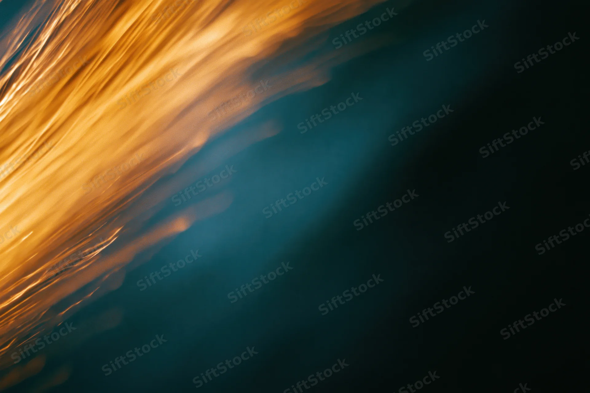 Warm amber light streaks moving diagonally across a dark background with blurred motion and bokeh effect