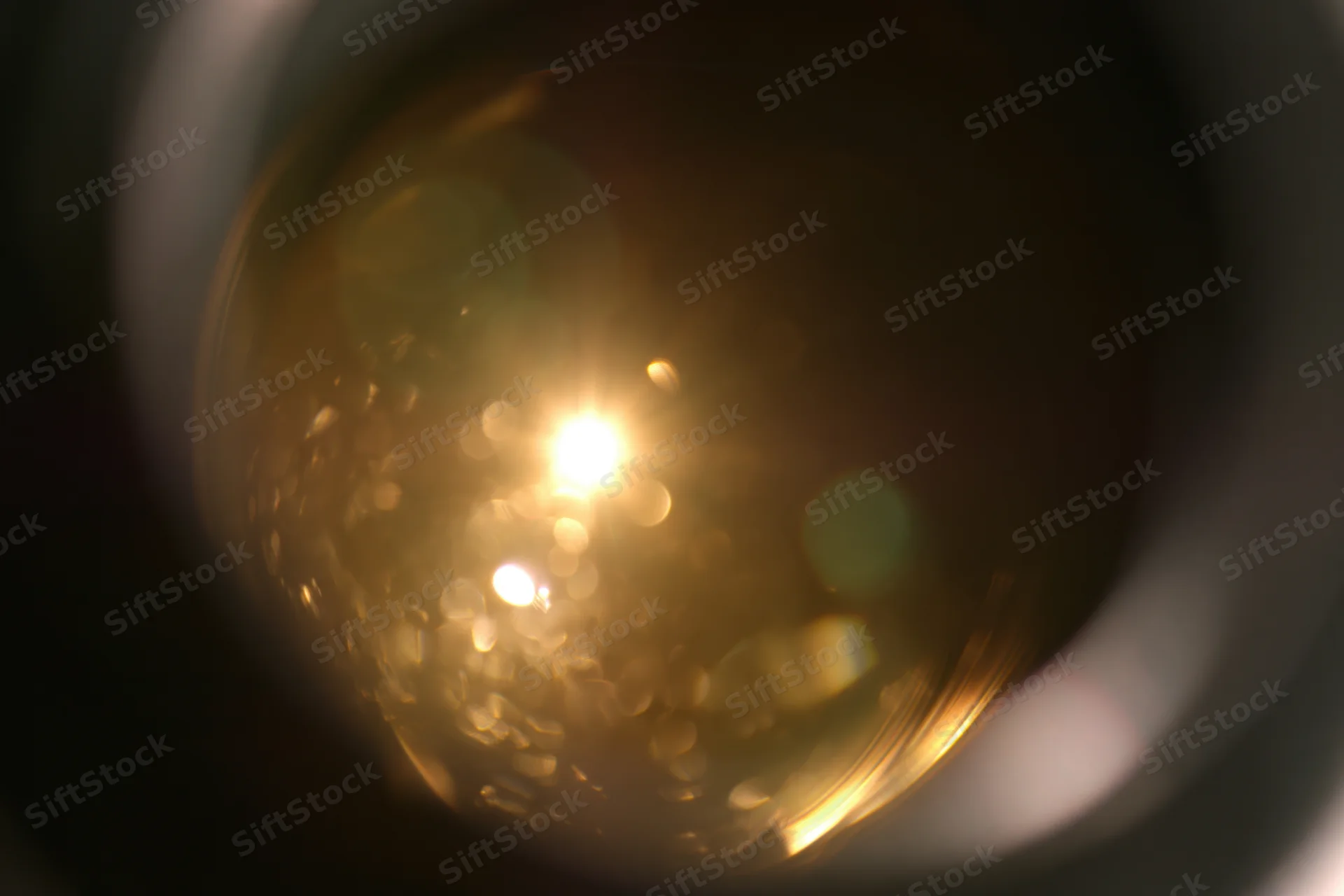 Close-up view through a camera lens showing golden bokeh light reflections and circular flares inside the aperture