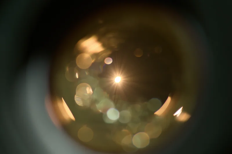 Close-up view through a camera lens showing bokeh lights and lens flare