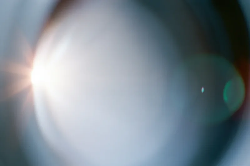 Extreme close-up of a camera lens element with bright light flare and bokeh effect