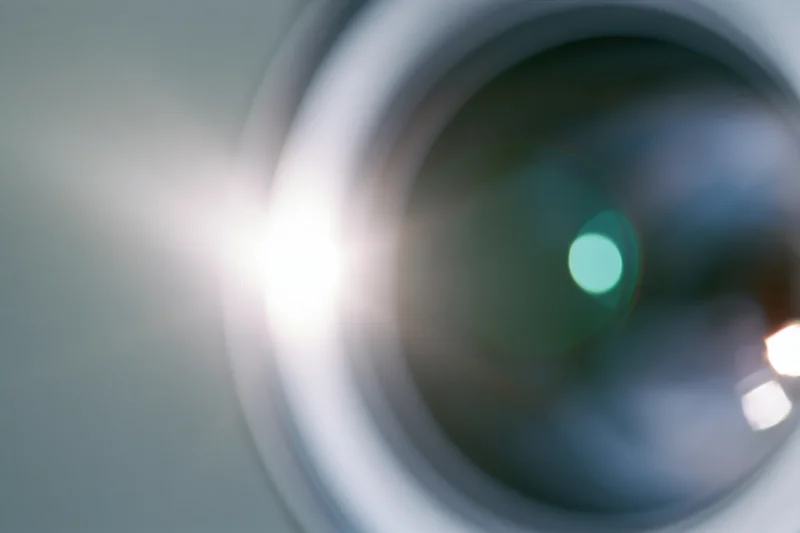 Extreme close-up of a camera lens element with bright light flare and reflections