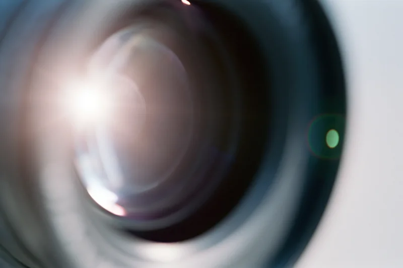 Extreme close-up of a camera lens element with bright light reflection and lens flare