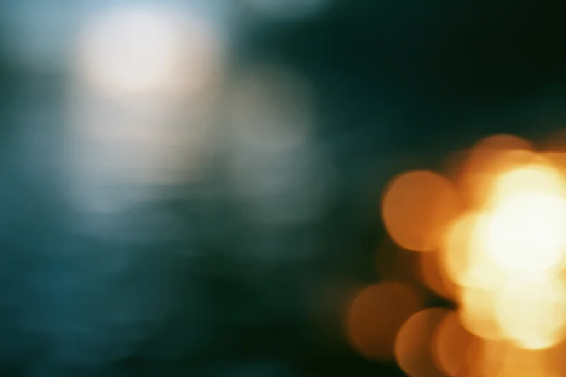 Blurred bokeh lights in warm tones against a dark teal background with soft glow and copyspace