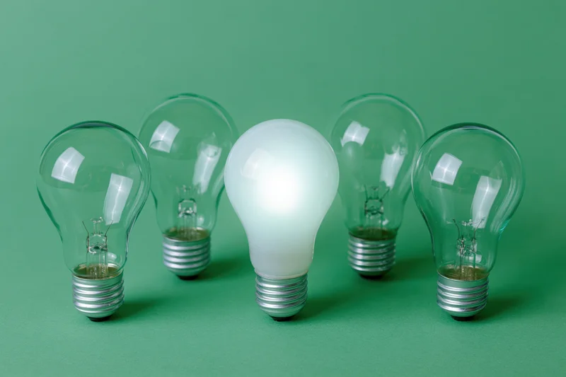 Five incandescent light bulbs arranged in a horizontal row on a green background with one illuminated and frosted in the center