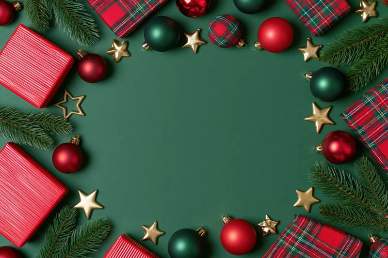 Christmas ornaments and wrapped gifts arranged in a flat lay with pine branches and gold stars on a green background