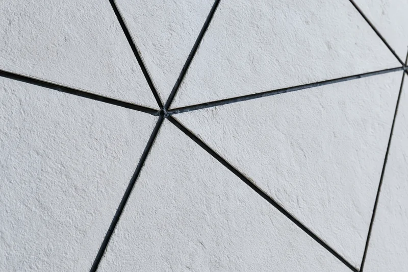 Textured concrete wall divided into irregular triangular sections by dark grout lines