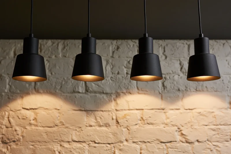 Four black industrial pendant spotlights hanging from ceiling above white brick wall