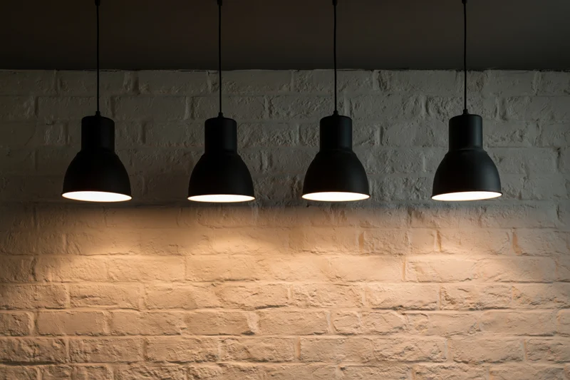 Four black industrial pendant lights hanging in a row above a white brick wall