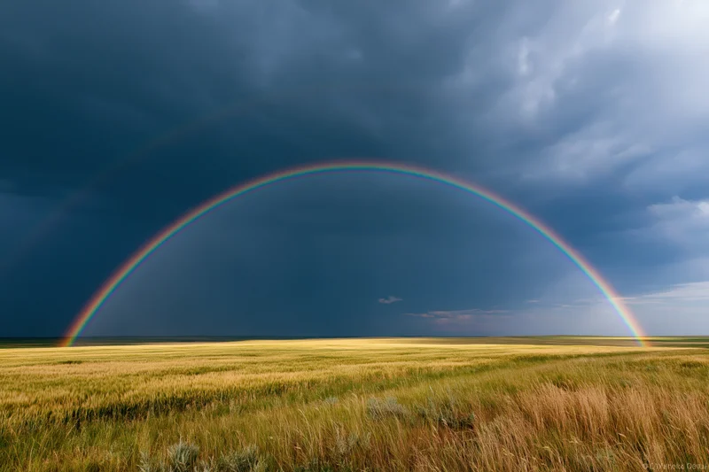 Double rainbow arching over flat prairie field under stormy sky