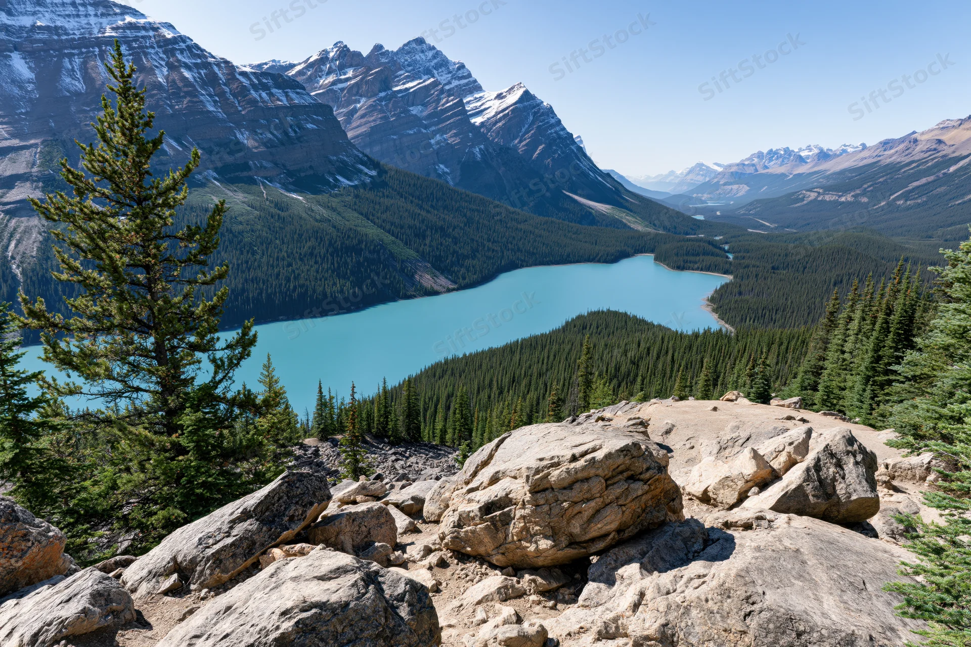 Glacial turquoise lake nestled in rocky mountain valley surrounded by pine forest and snow-capped peaks