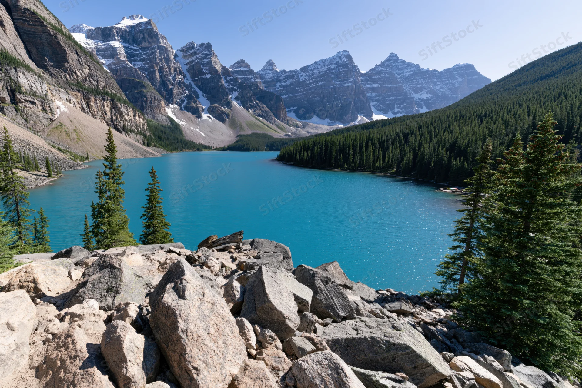 Glacial turquoise lake nestled in rocky mountain valley surrounded by pine forest and snow-capped peaks