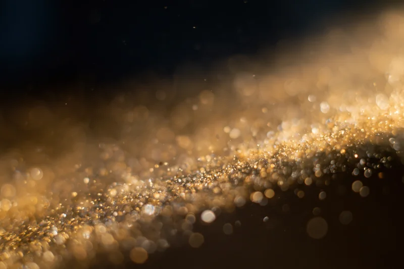 Gold dust particles and light orbs suspended midair in a soft glowing abstract background