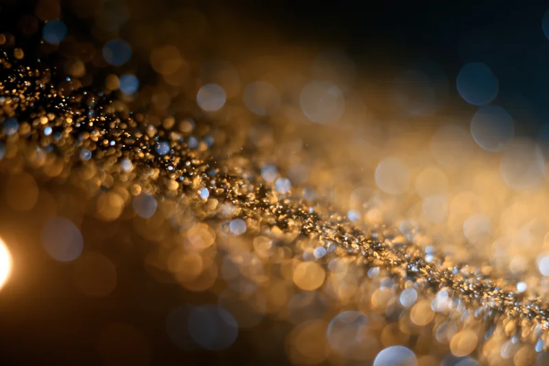 Gold dust particles suspended mid-air with bokeh light orbs in warm ambient glow