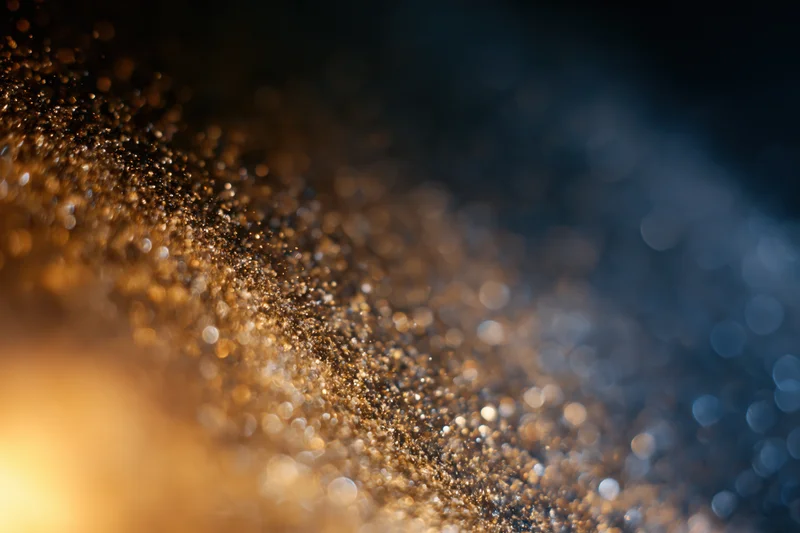 Gold dust particles suspended mid-air with bokeh light orbs in a gradient background