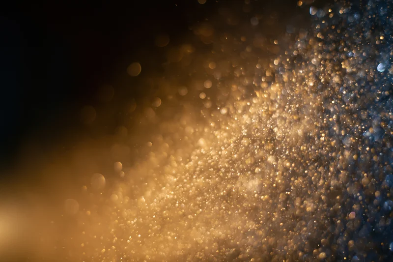Gold dust particles and light orbs suspended midair in a warm glowing abstract background