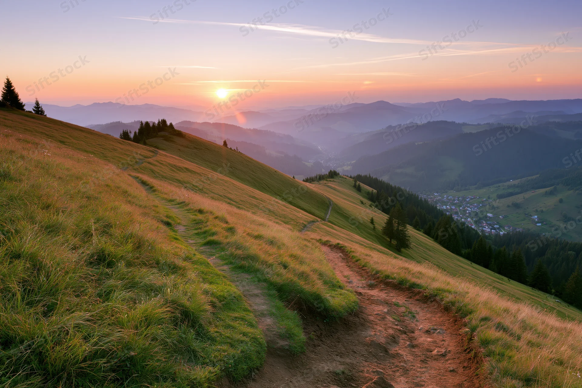 Grassy mountain hillside with a curving dirt path descending into a valley at sunset