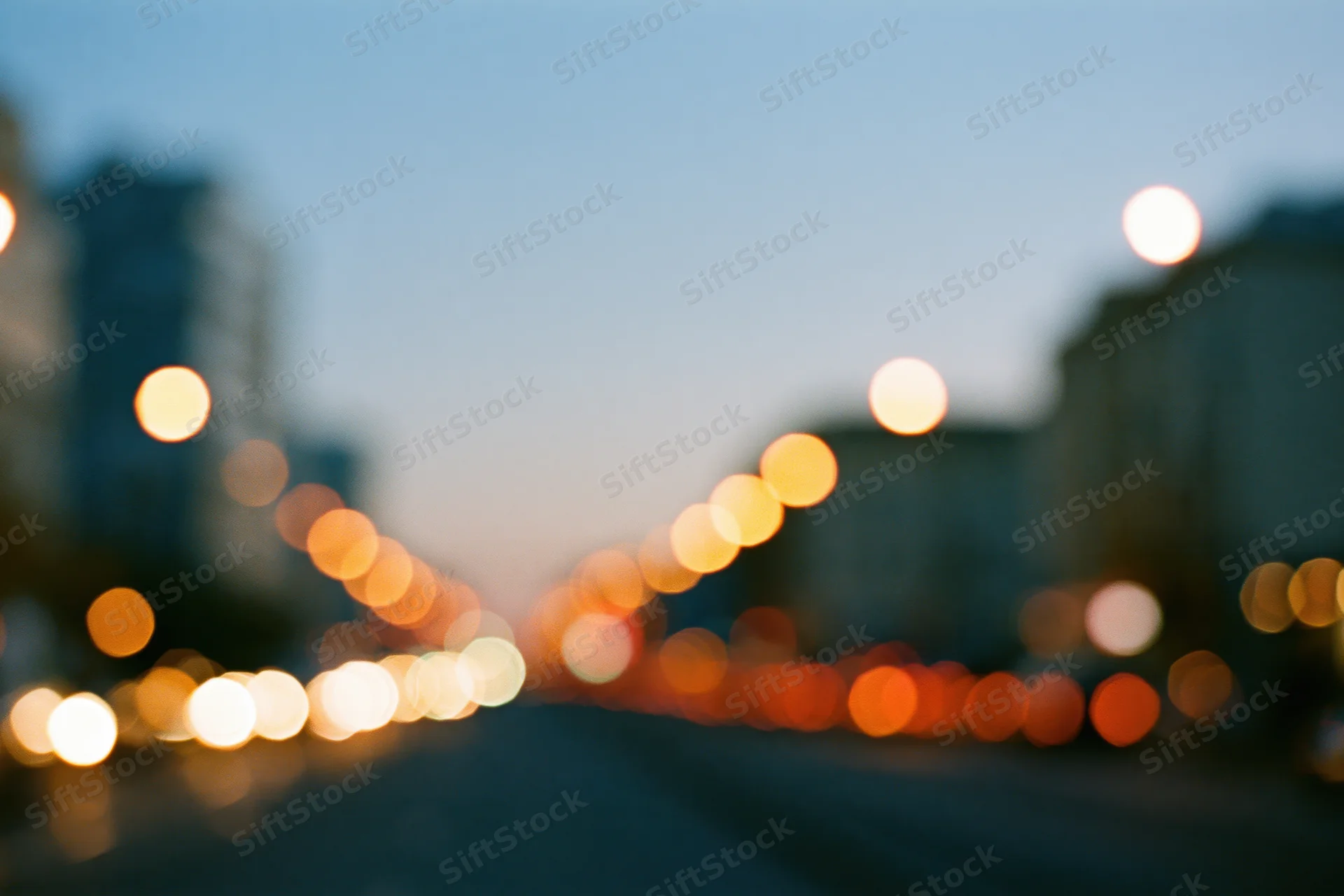 Defocused city street at dusk with bokeh lights from traffic and buildings