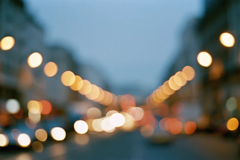Defocused city street at dusk with glowing bokeh lights from traffic and streetlamps