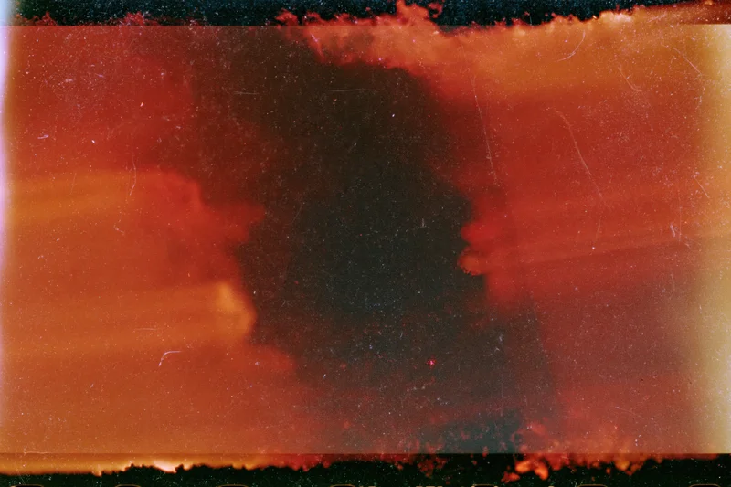Abstract analog photograph with heavy light leak and underexposure showing warm red and orange tones with dark central shadow