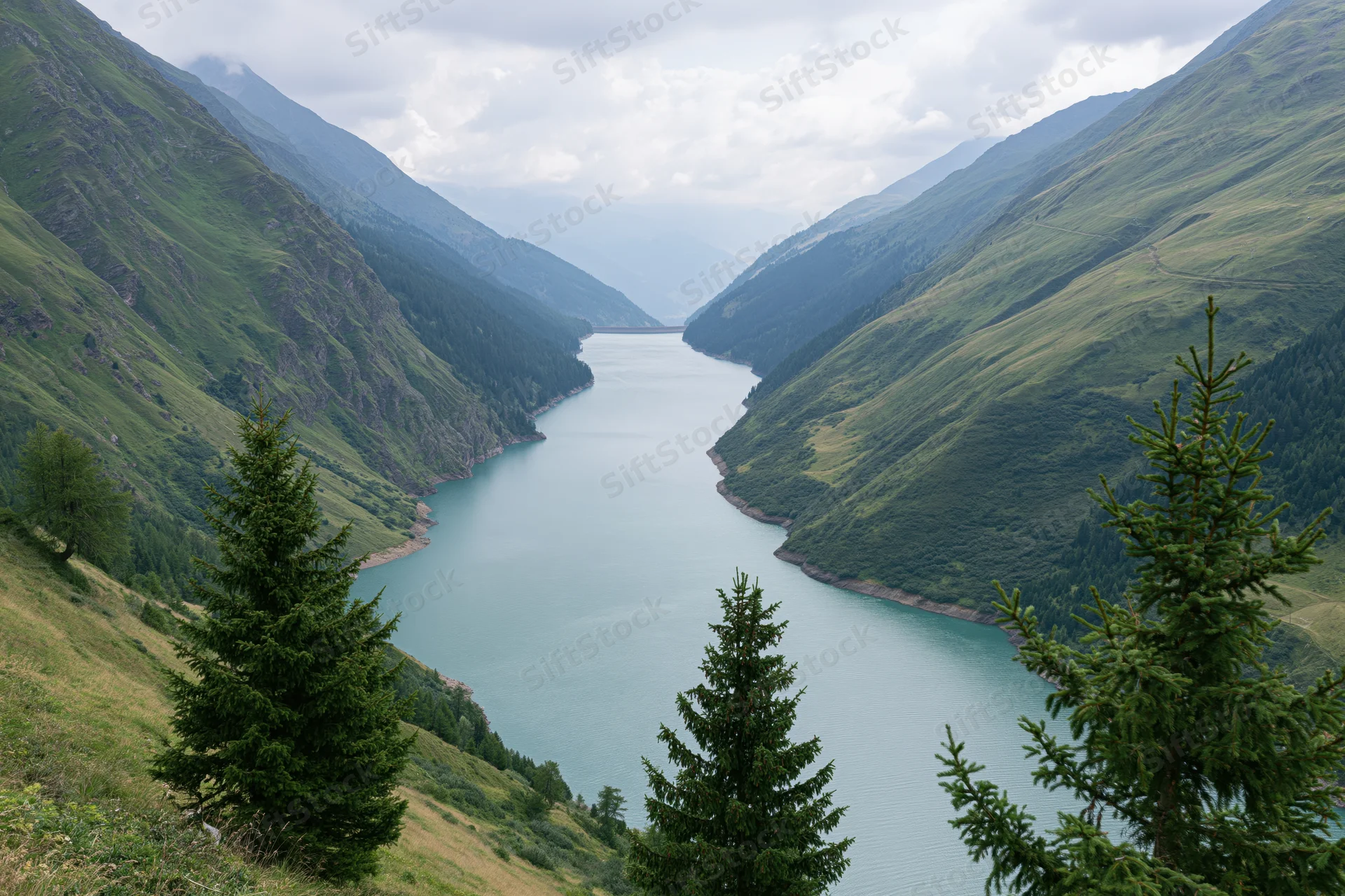 Reservoir nestled between steep green mountains under cloudy sky