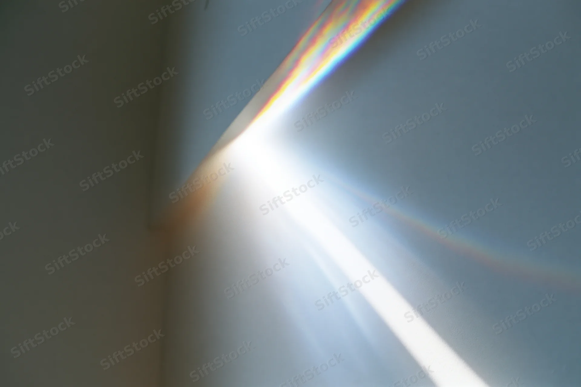 Intense lens flare and rainbow spectrum projected across a white wall corner in an indoor space