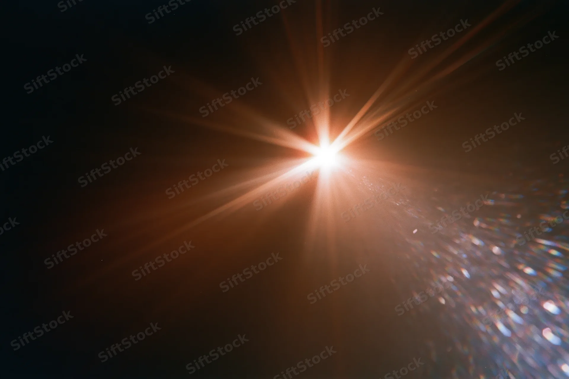 Intense lens flare from a bright light source radiating starburst beams across a dark background with sparkling particles on the right