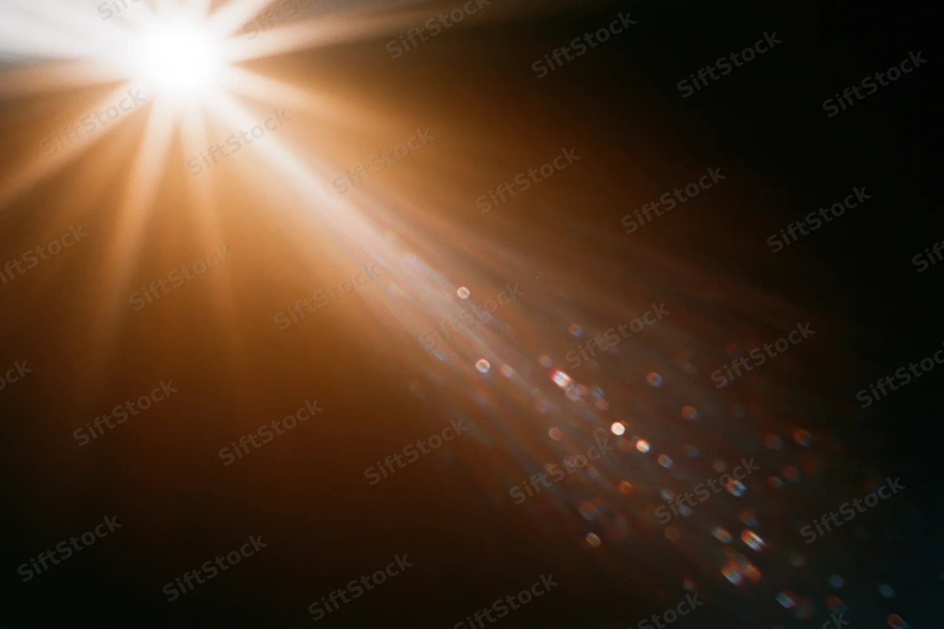 Intense lens flare from a bright light source casting radiant beams and sparkling particles across a dark background